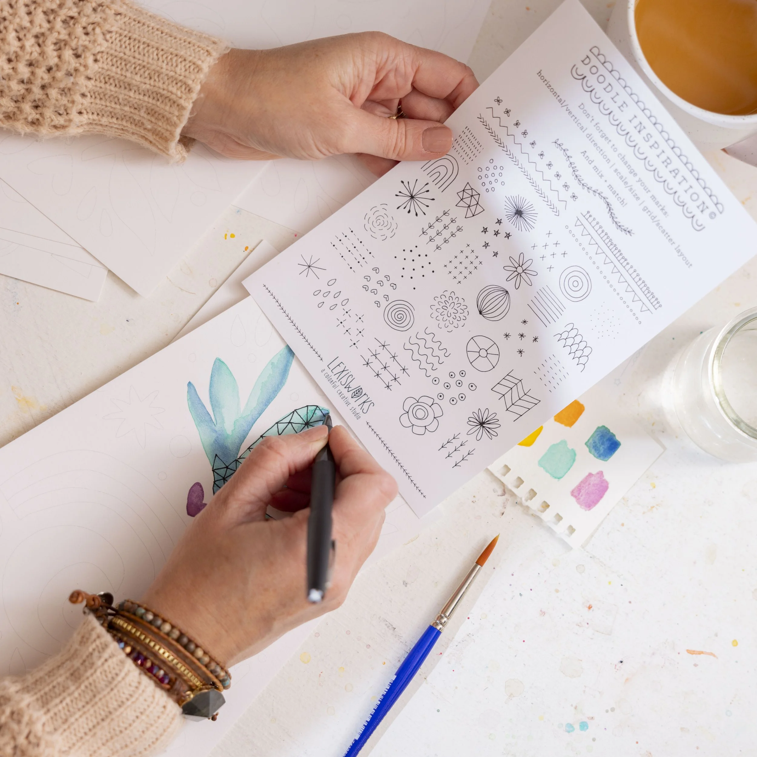 Hands holding an art print and a marker, surrounded by drawing supplies, offering a doodle inspiration guide with various doodle patterns and a watercolor pineapple illustration.