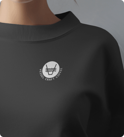 Close-up of a black sweatshirt with a white circular logo that says 'Vessel Craft Coffee' and features a stylized coffee cup with steam.
