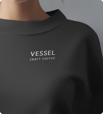 Close-up of a person wearing a dark gray sweatshirt with the text 'VESSEL CRAFT COFFEE' on the chest.