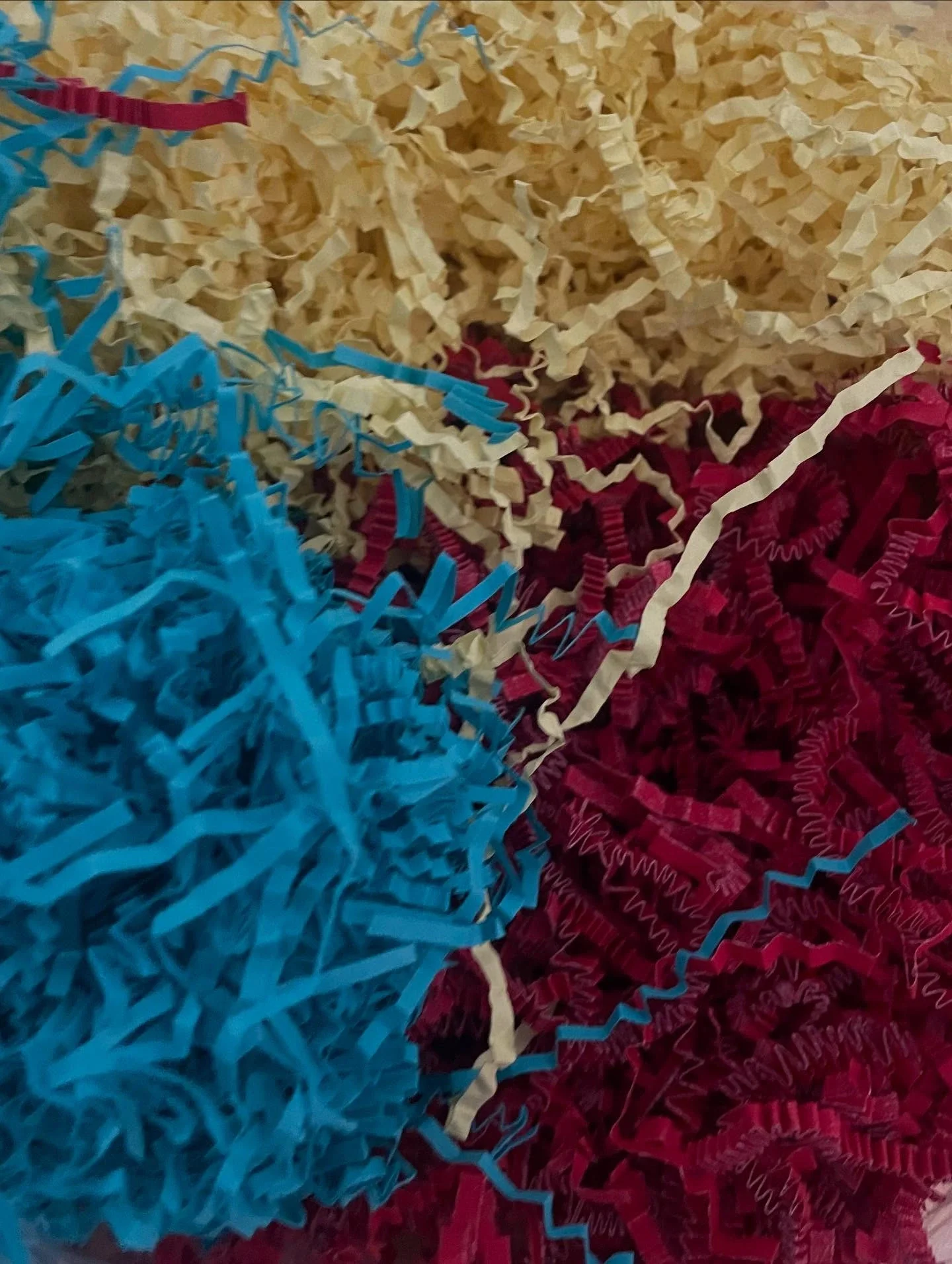 Shredded paper in vibrant red, yellow, and blue hues, forming a colorful pile of packaging material.