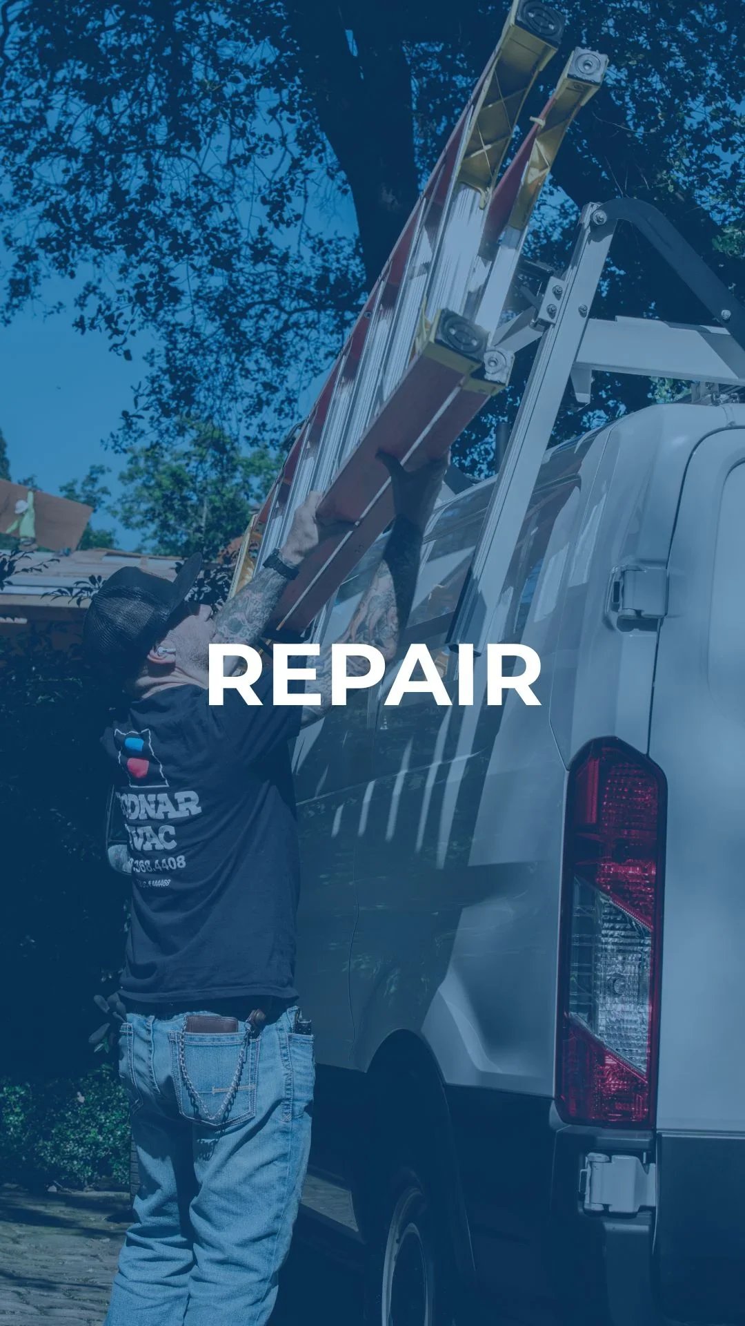 A repair technician with tattoos, wearing a black baseball cap and a black T-shirt, fixing or inspecting a ladder on the back of a white pickup truck parked outdoors under a blue sky and trees.