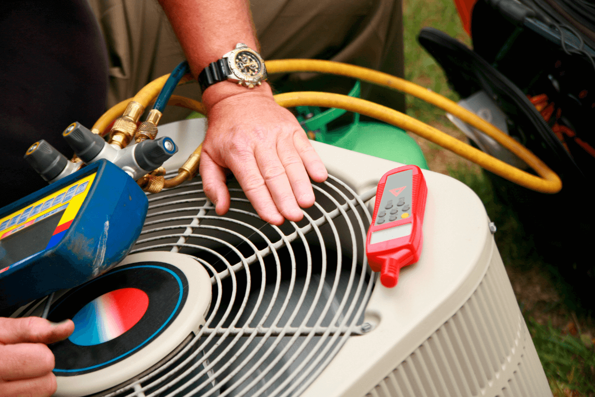 A close-up of a technician's hand checking an A/C condenser unit with diagnostic gauges and a multimeter, used on the Bodnar HVAC website to represent our free second opinions and expert, repair-first diagnostics in the Mid-Peninsula.