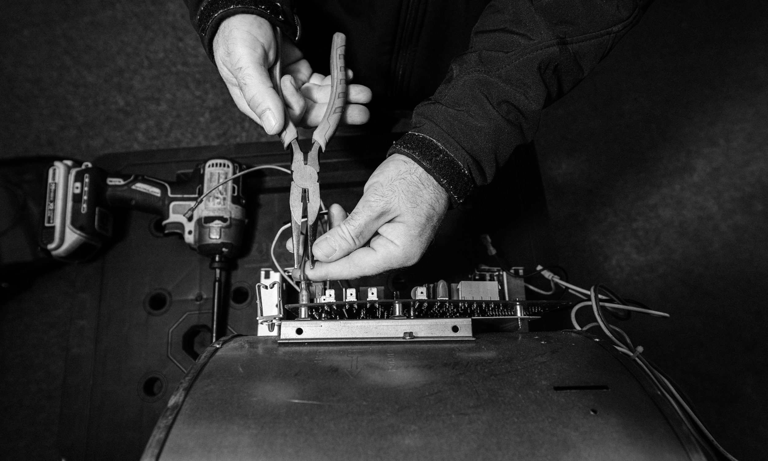 Close-up of an HVAC technician using needle-nose pliers to perform precision electrical repairs on a furnace control board.