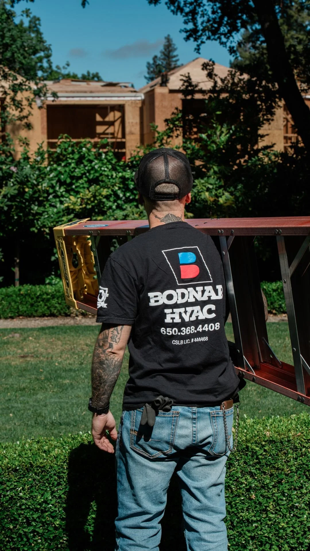 A Bodnar HVAC technician carrying a ladder toward a residential project, showcasing professional service and branding.