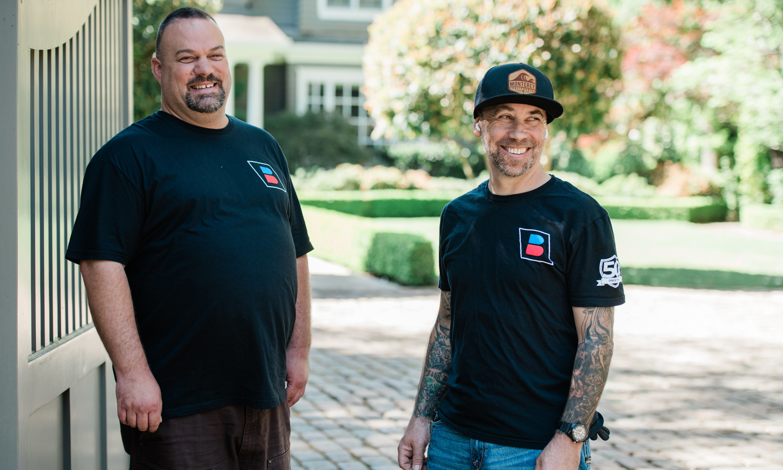 Two professional HVAC technicians from Lamb's Heating and Cooling smiling in front of a residential home.
