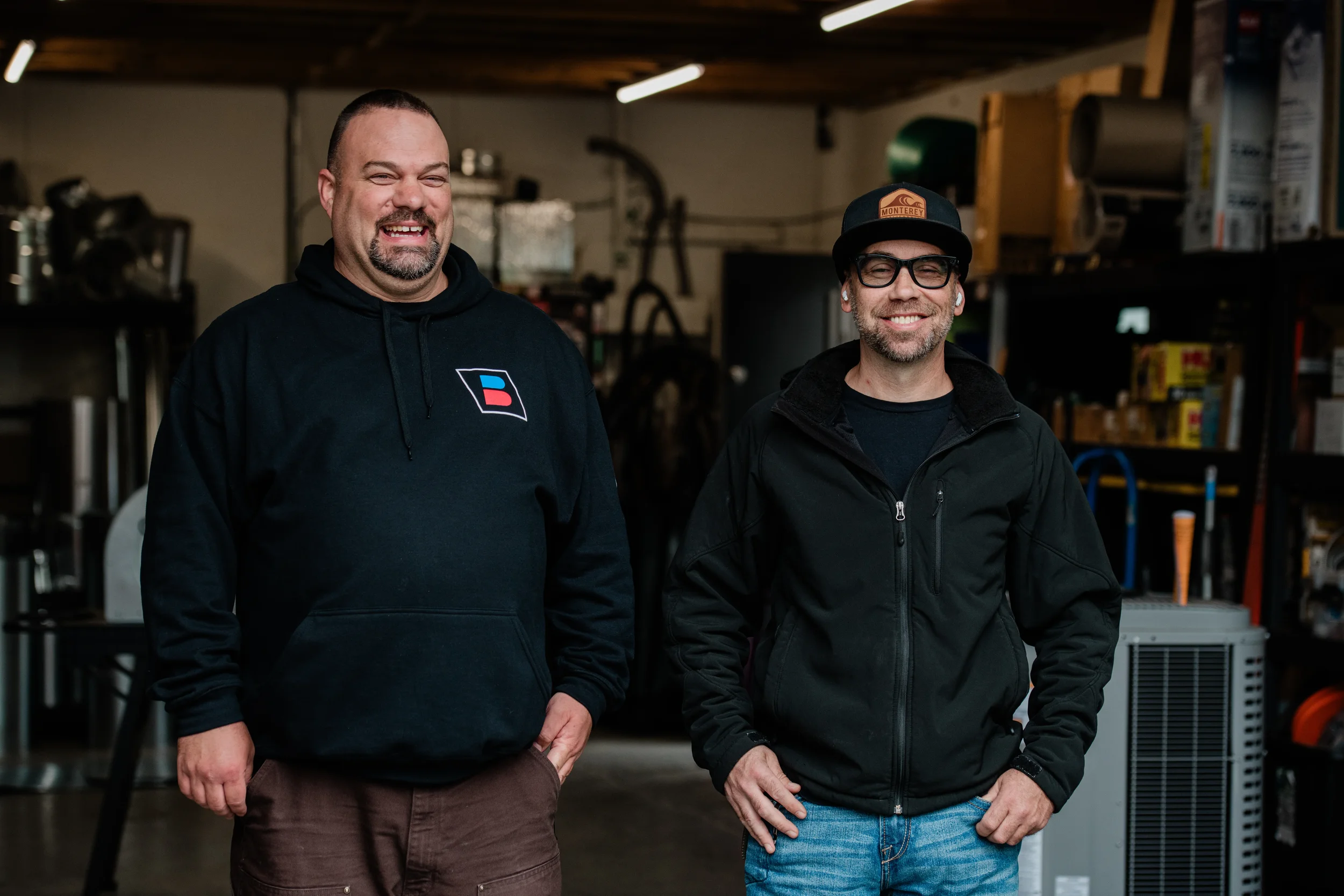 Two professional HVAC technicians from Lamb's Heating and Cooling smiling in front of a residential home.