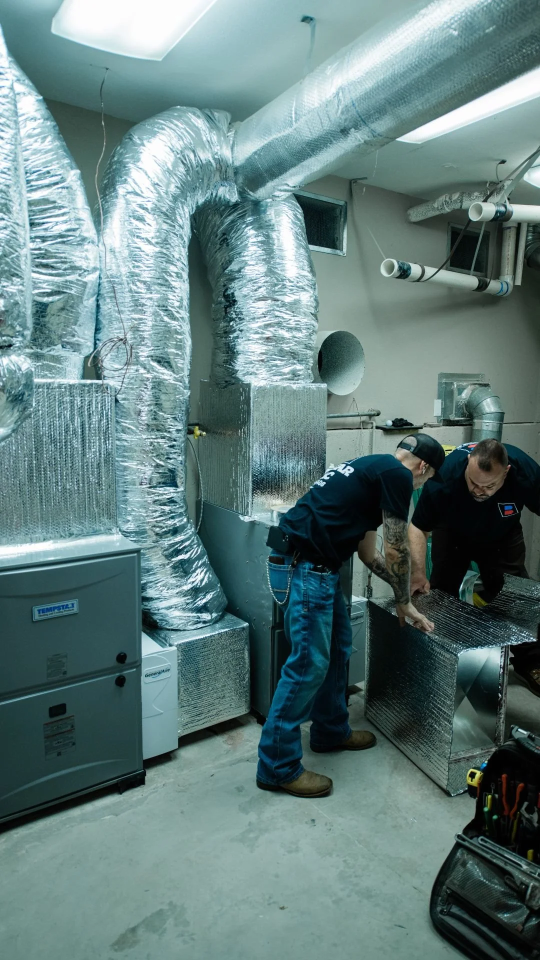 Two Bodnar HVAC installation specialists professionally fitting custom ductwork and a new furnace system in a residential mechanical room.