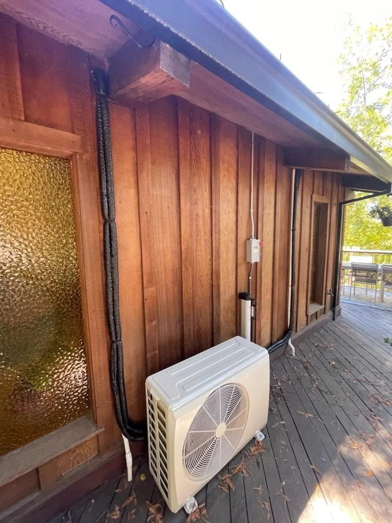 Outdoor ductless mini-split heat pump unit installed on a residential deck in Woodside, CA, featuring clean, black-insulated refrigerant lines tucked against natural wood siding.