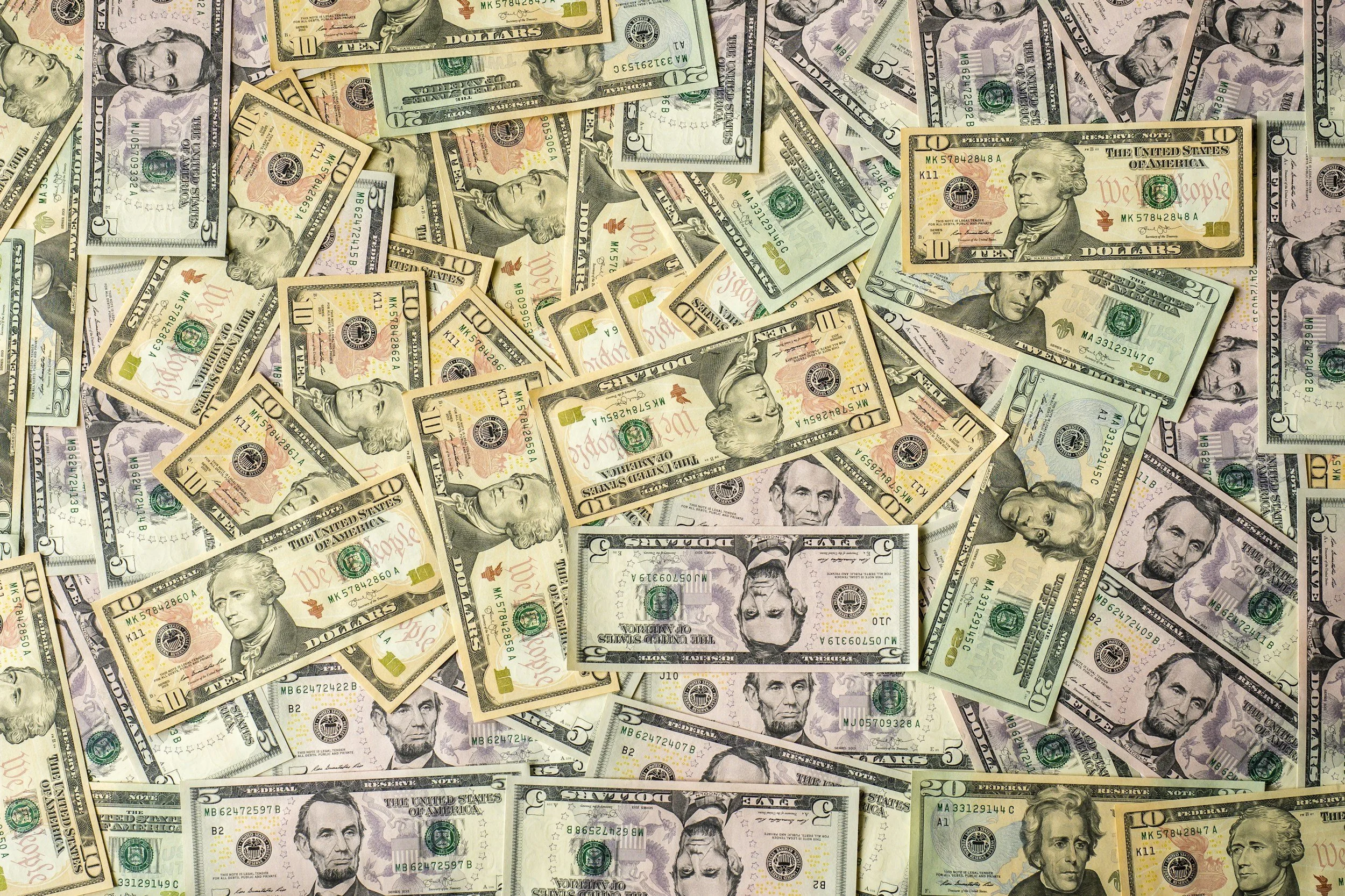 A large amount of US paper currency, including $5, $10, $20, and $50 bills, scattered across a surface.