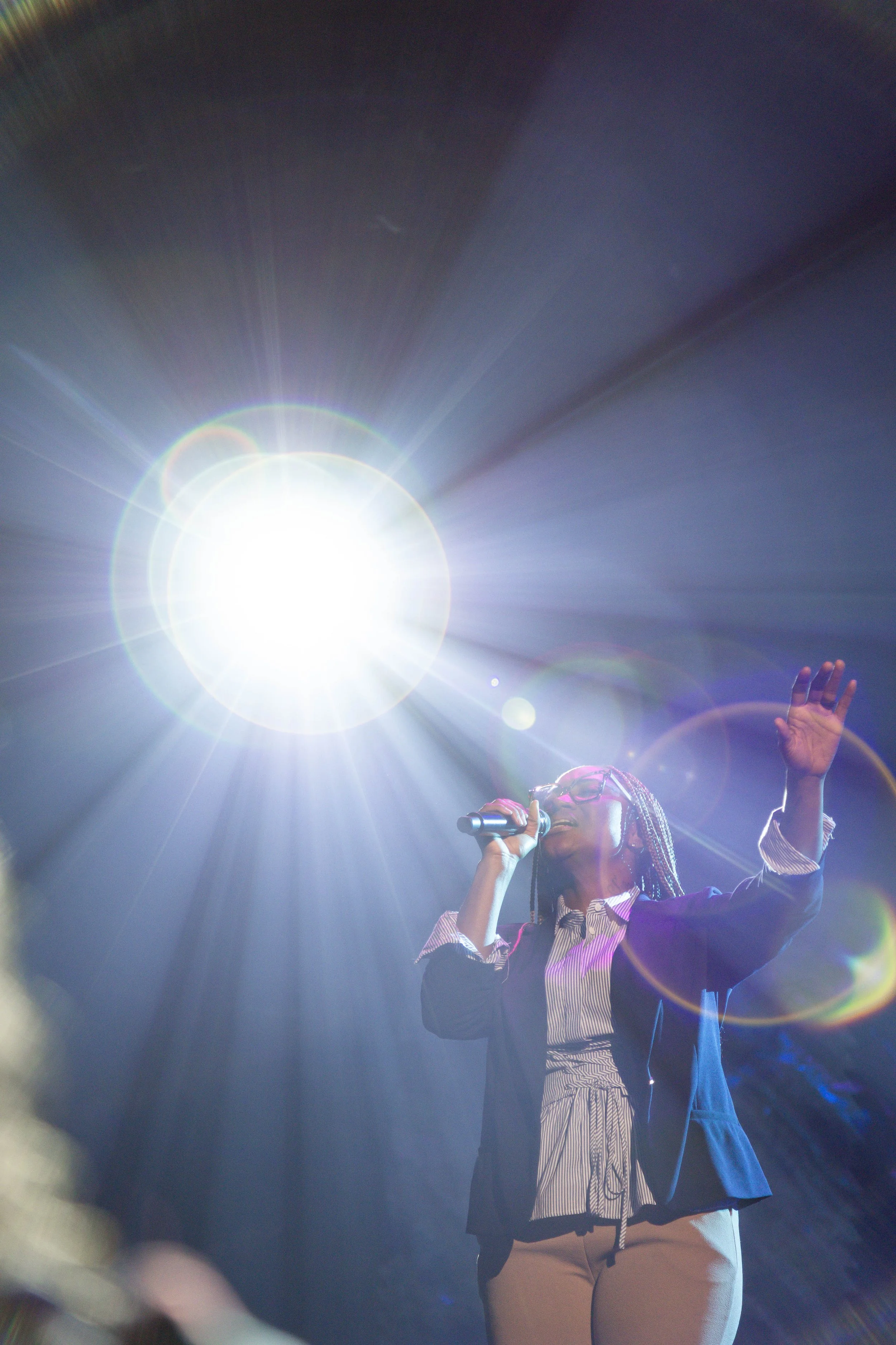 A woman singing into a microphone with bright stage lights and lens flares.
