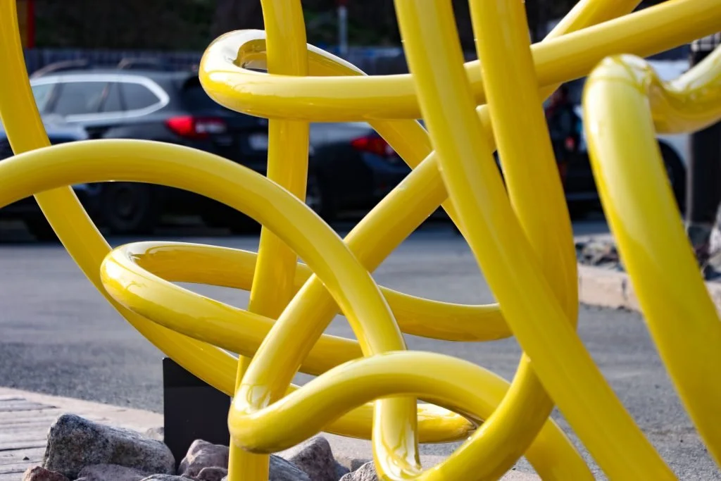 A close-up shot showing the detail of a large yellow steel sculpture resembling three knots.