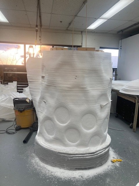 A large, white sculpture of a mitten in progress stands in a workshop.