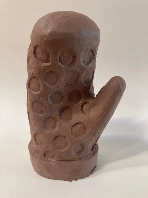 A brown clay sculpture of a mitten with circular designs throughout.