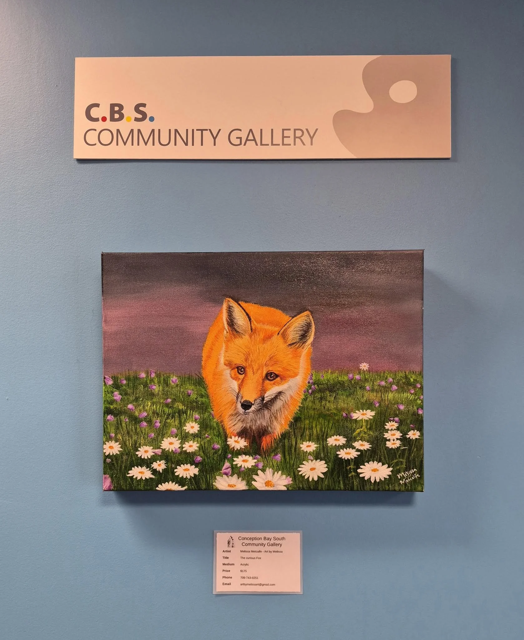 A painting of a fox walking through a field of daisies and wildflowers hangs on a light blue wall with a small card underneath. Above is a white sign that says "C.B.S. Community Gallery."