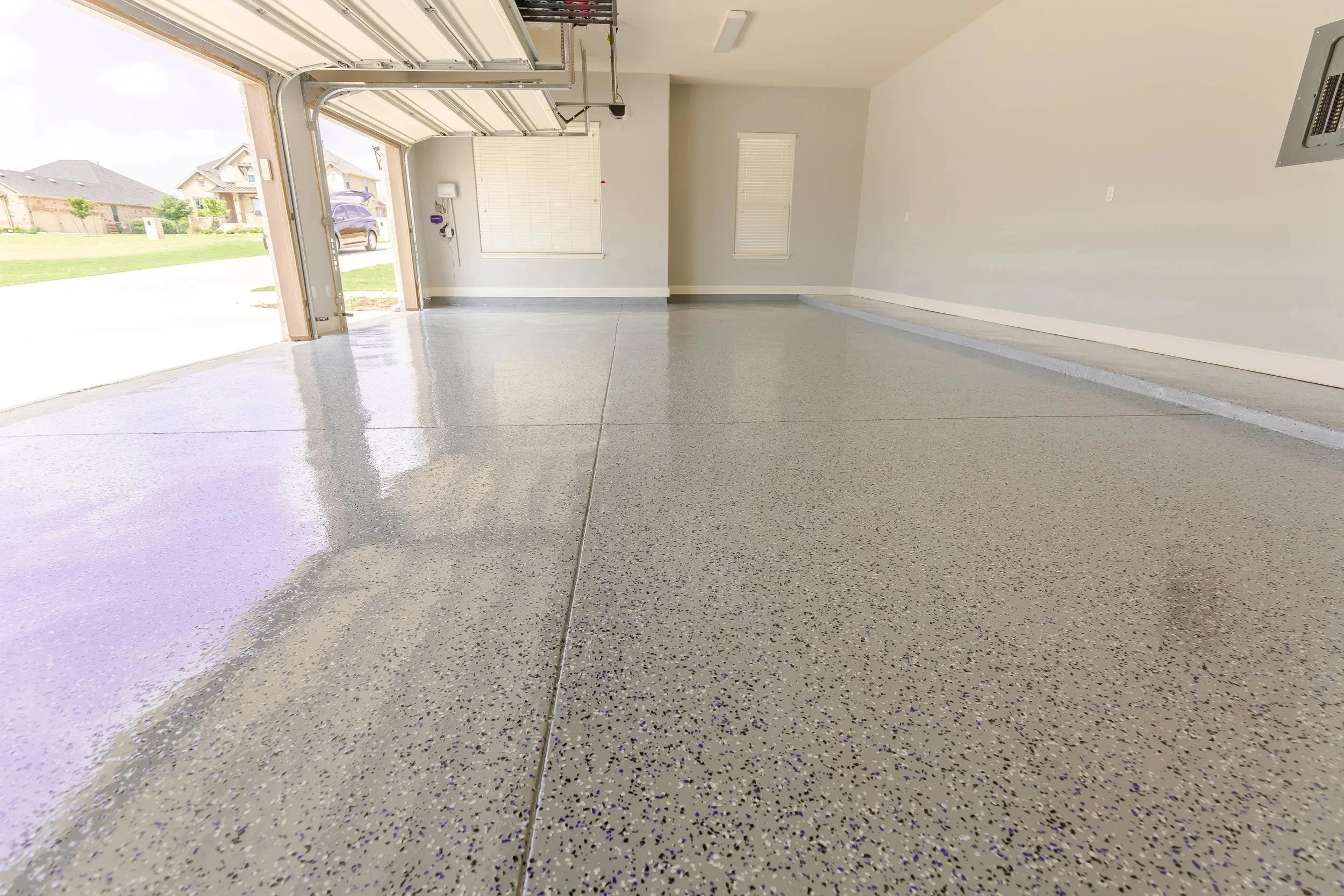 Empty garage with freshly sealed and polished concrete floor, some sunlight coming in through open garage door.