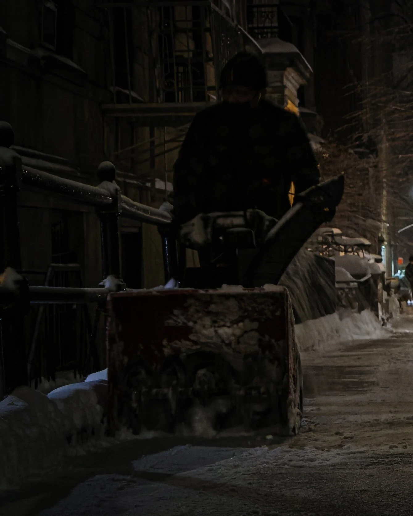 Person using a snowblower on a snowy Calgary sidewalk at night
