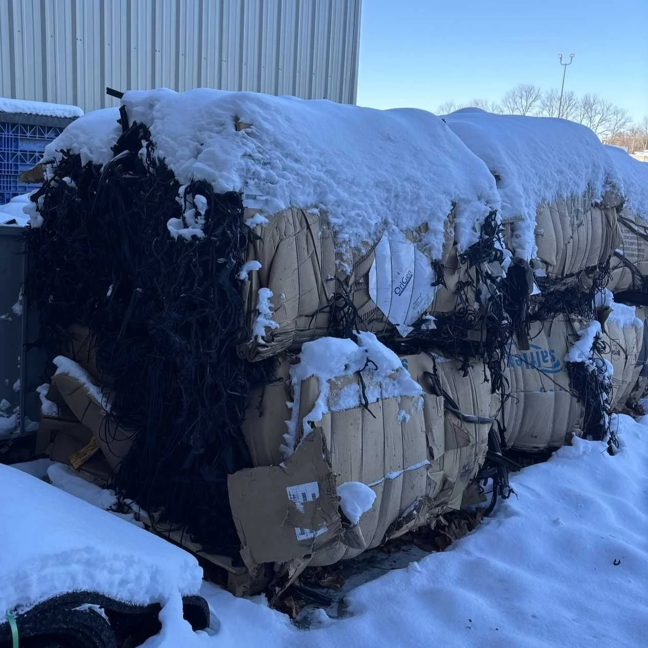 Bales of EPDM secured with cardboard sheets for bale integrity stored outside and covered in snow