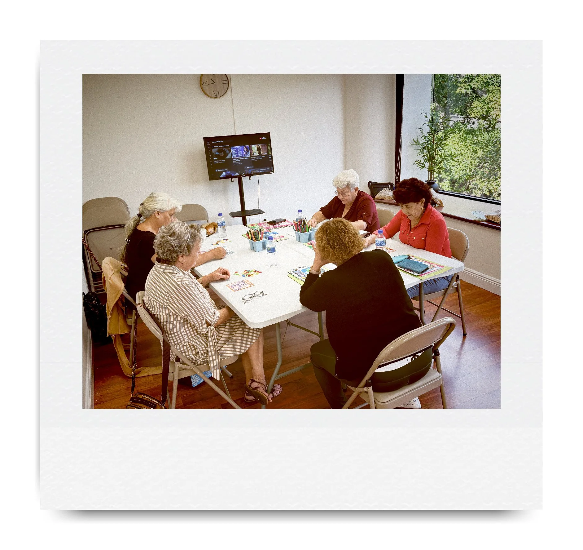 Group of older adults seated around a table engaging in crafts with art supplies in a bright room.