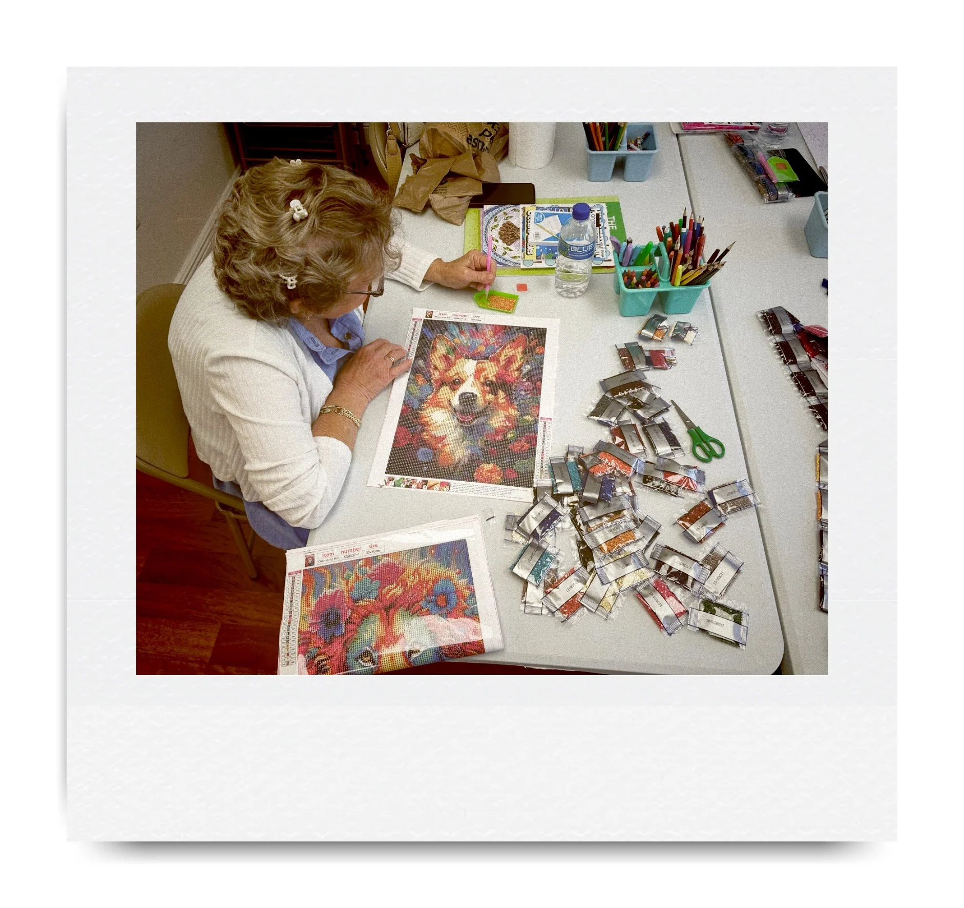 Person assembling a colorful puzzle featuring a dog, surrounded by puzzle pieces and art supplies on a table.