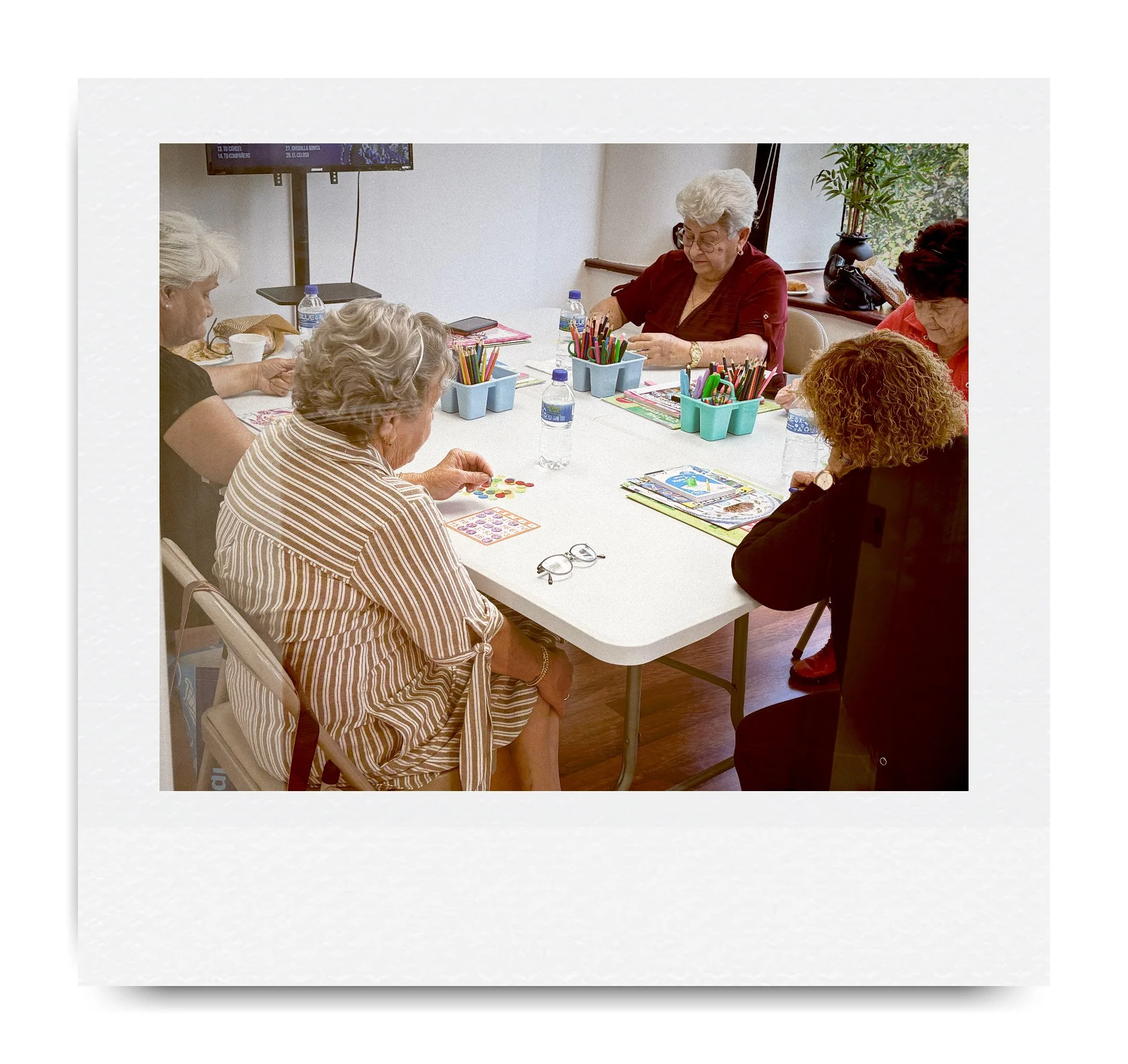 Group of elderly individuals engaged in arts and crafts at a table, with coloring books and drawing supplies.