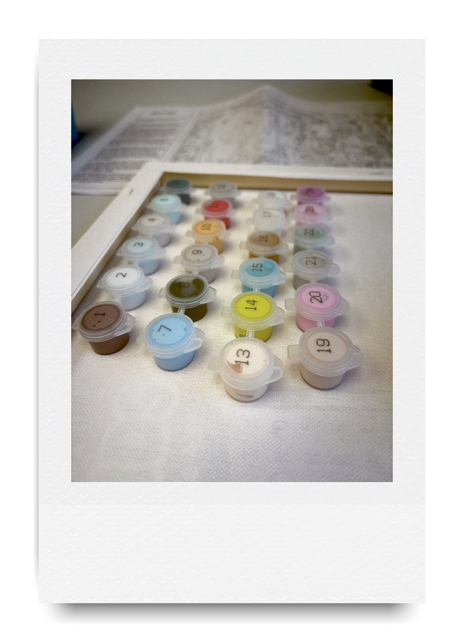 Small plastic paint pots numbered and arranged on a table, likely part of a paint-by-numbers kit.
