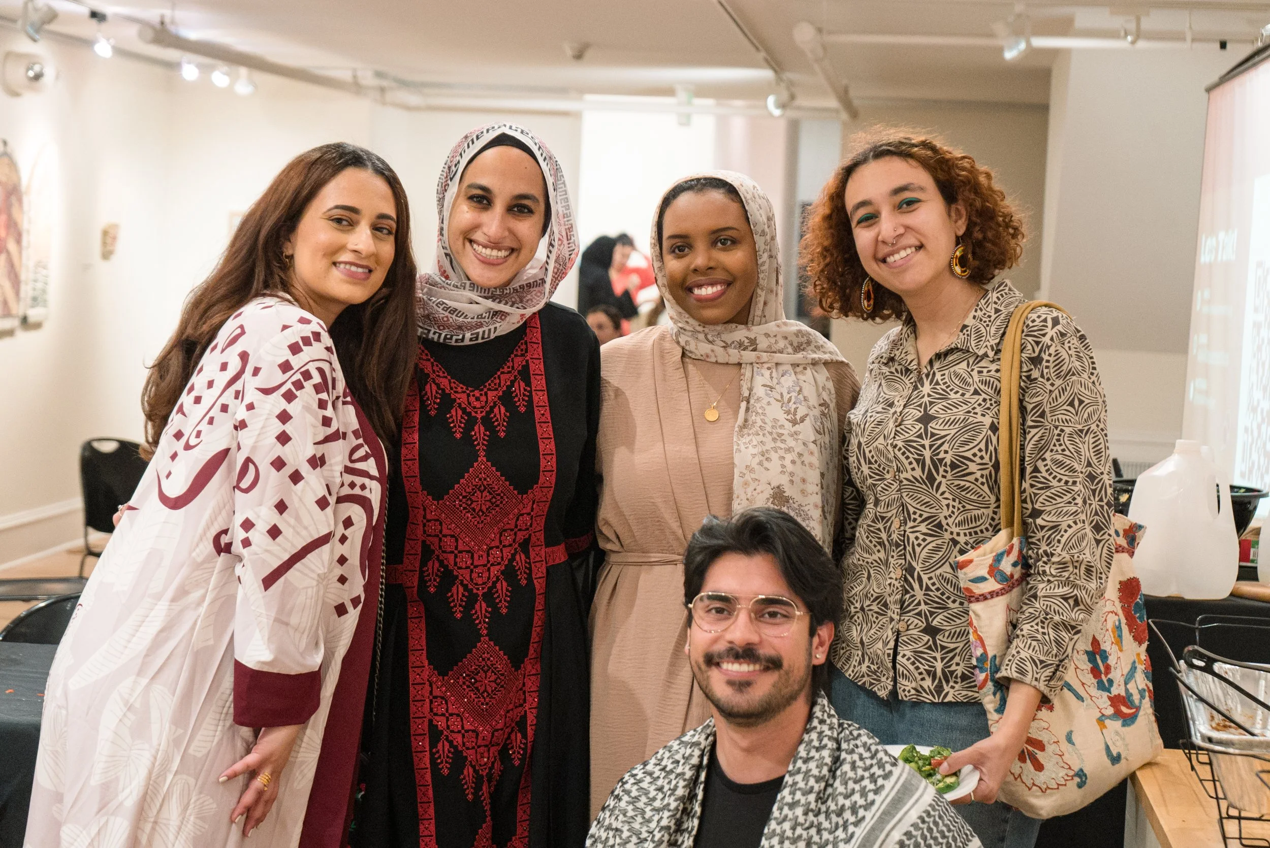 Group of five diverse women and one man smiling at a gathering or event in an indoor setting.