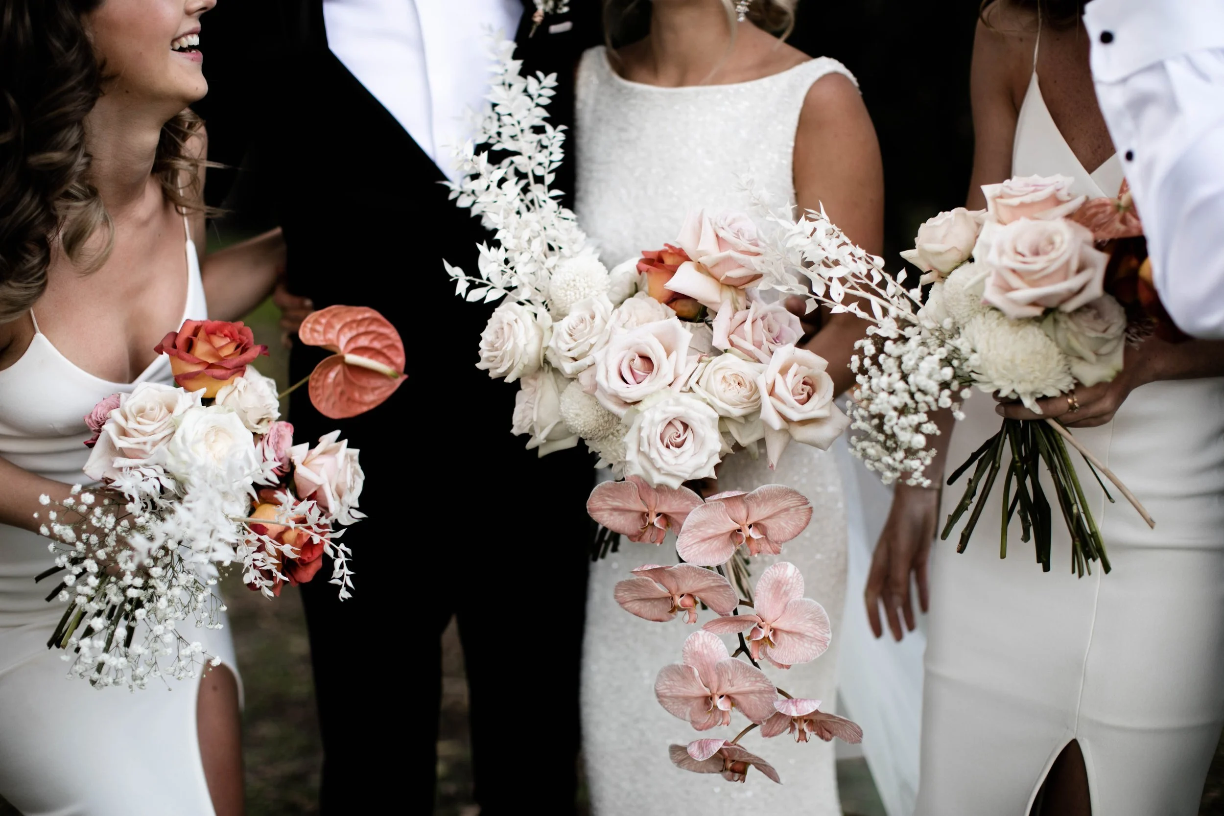 Women in wedding dresses holding bouquets of pink, white, and peach roses, orchids, and other flowers in a close-up moment during a wedding ceremony. Avenue Studio Co. Surrey Hills. Melbourne. Wedding in style.