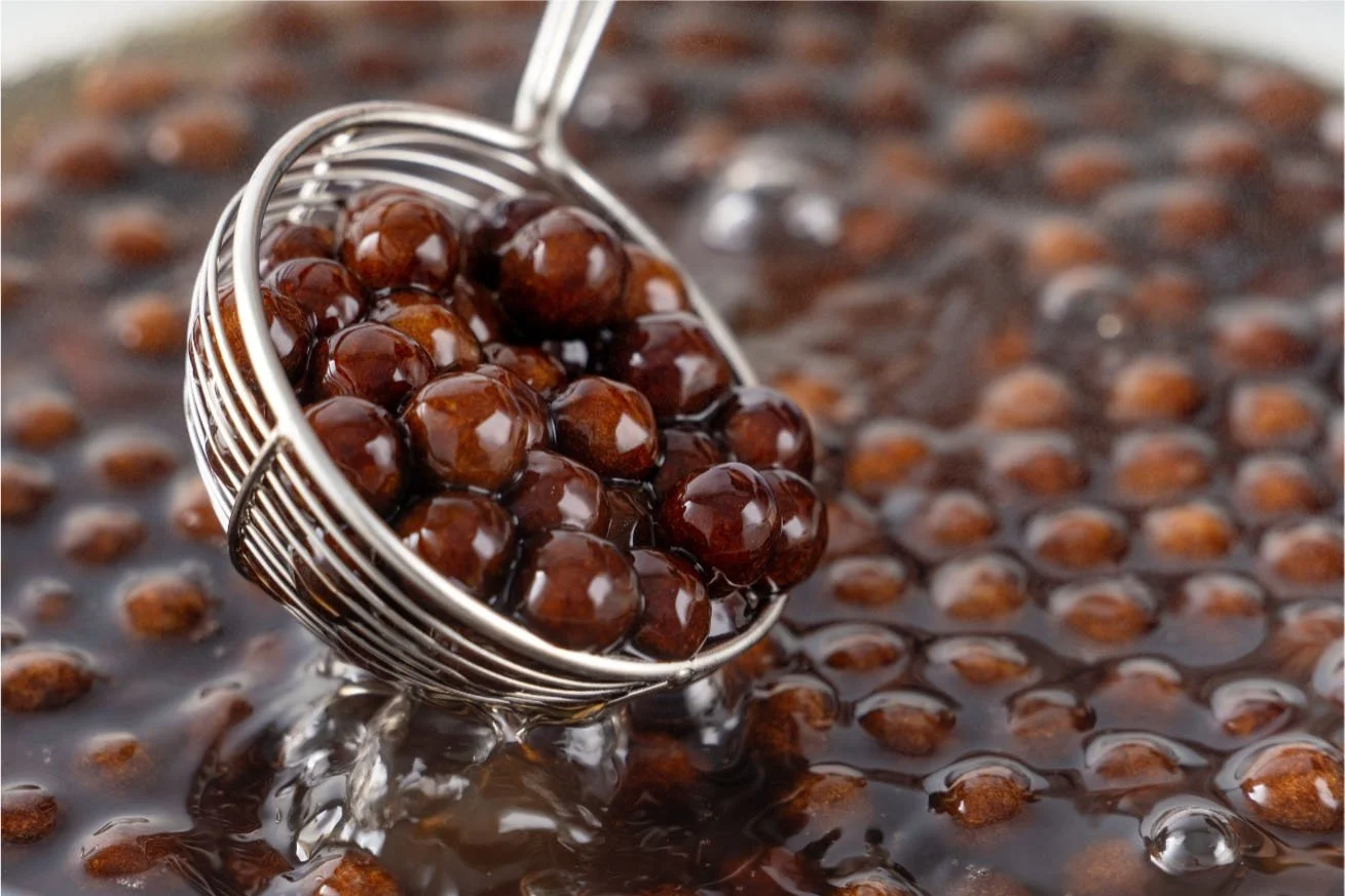 Cooked tapioca pearls and colorful toppings displayed in stainless steel pans