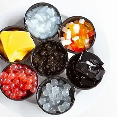 Six small bowls containing different types of colorful jelly and tapioca pearls on a white surface.