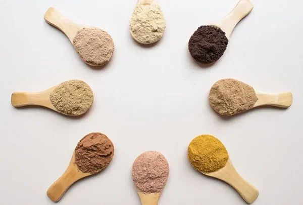 Eight wooden spoons filled with different colored powders arranged in a circle.