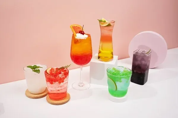 Five colorful layered beverages displayed on a white table — representing brand creativity, drink diversity, and global export capacity