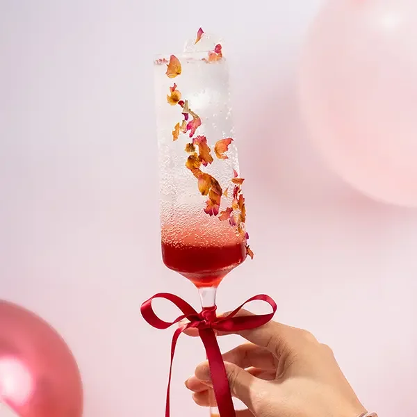 Rose syrup sparkling drink in a champagne glass with red-white gradient and rose petals, elegant floral cocktail style.