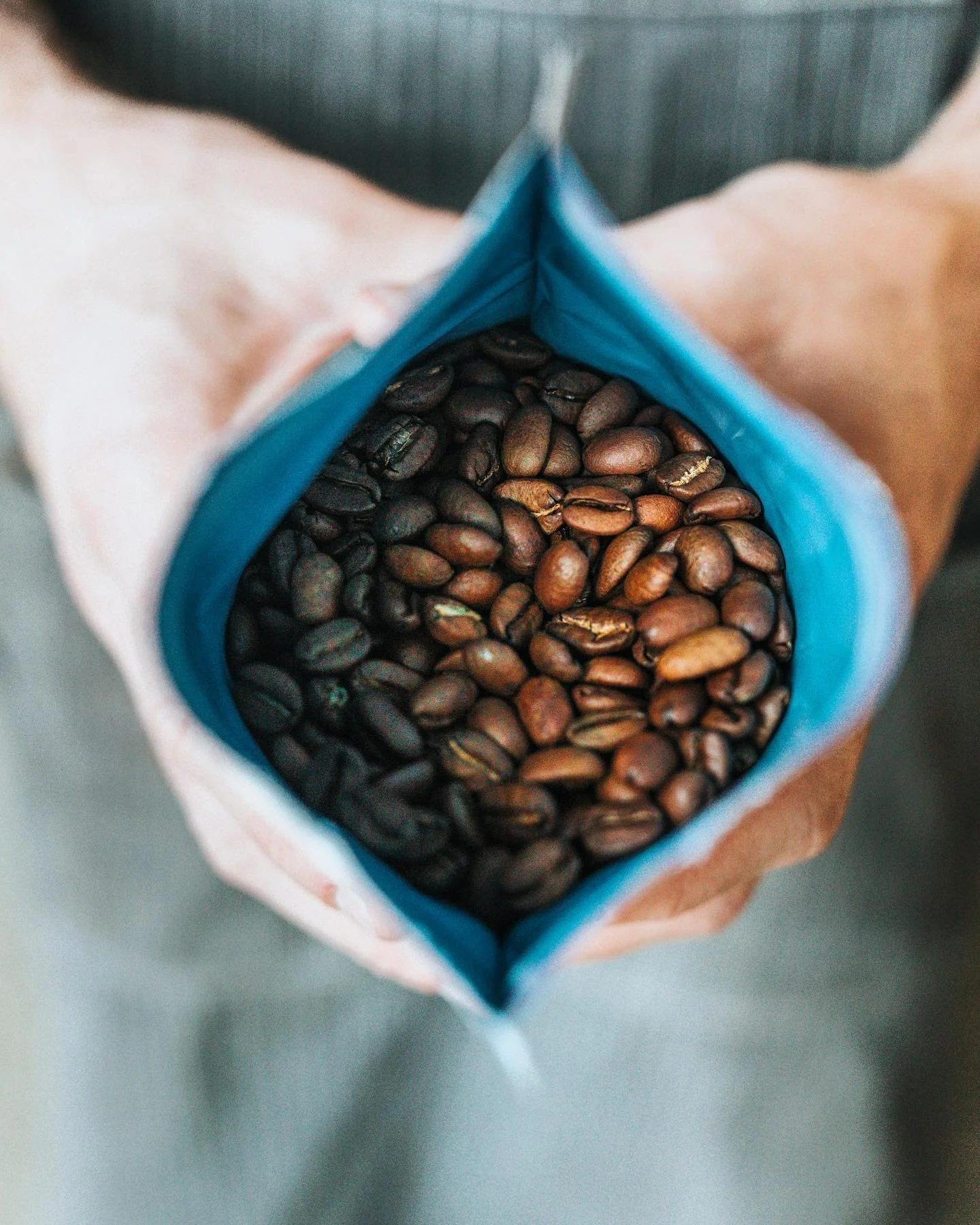 Close-up of an open blue coffee bean bag filled with dark brown roasted coffee beans.