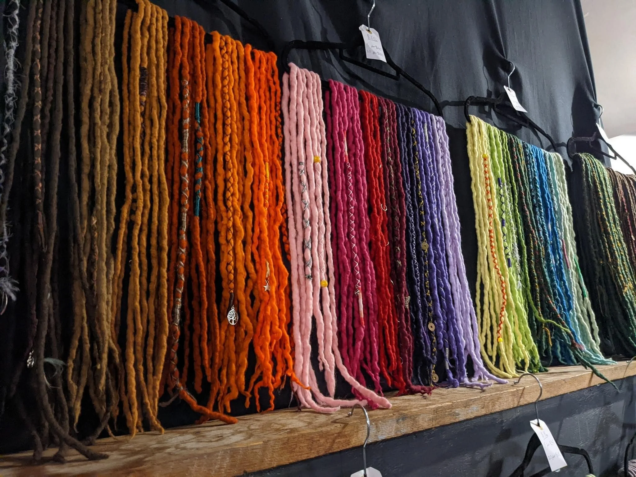 A display of colorful yarns arranged vertically in rainbow order on a black background, with some necklaces hanging among them.