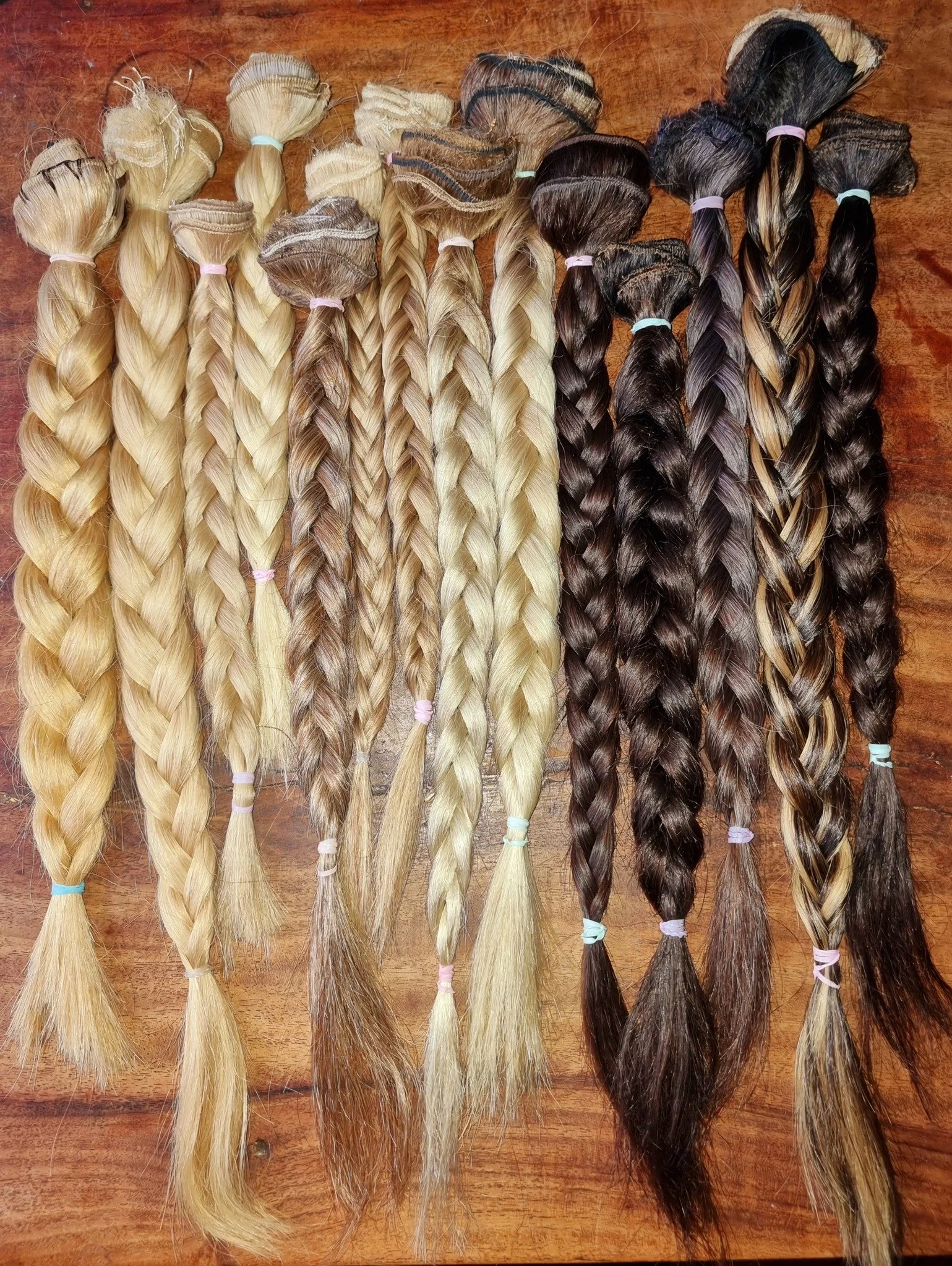 Multiple bundles of braided hair extensions in varying shades from blonde to dark brown, laid out on a wooden surface.