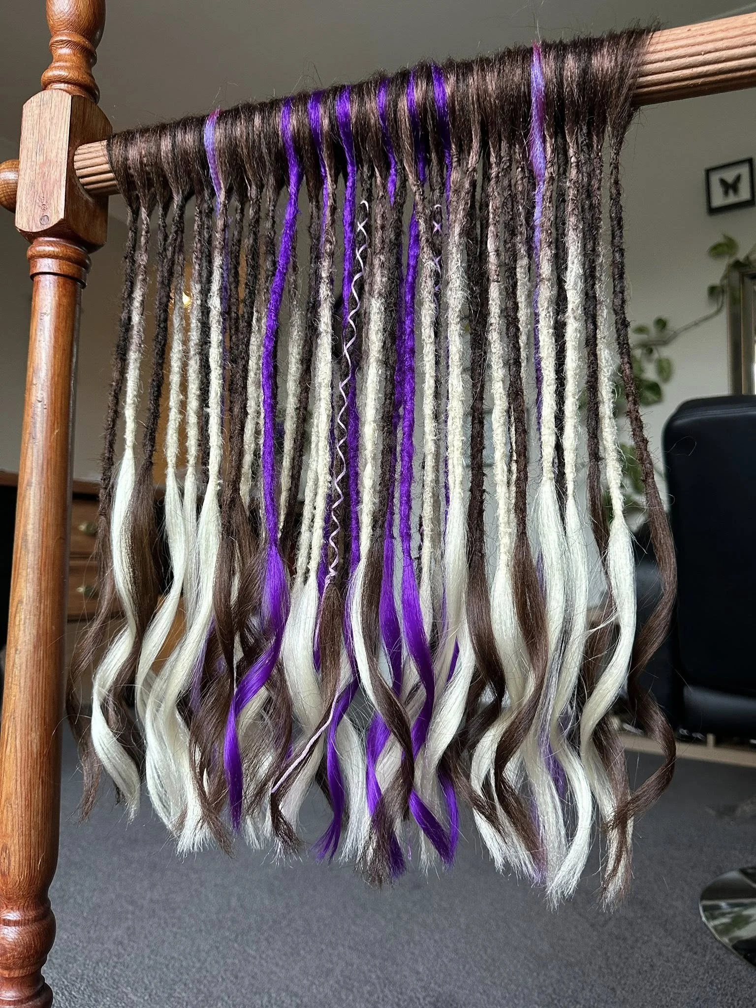 A wooden knitting loom with strands of yarn in shades of black, white, purple, and gray hanging from it.