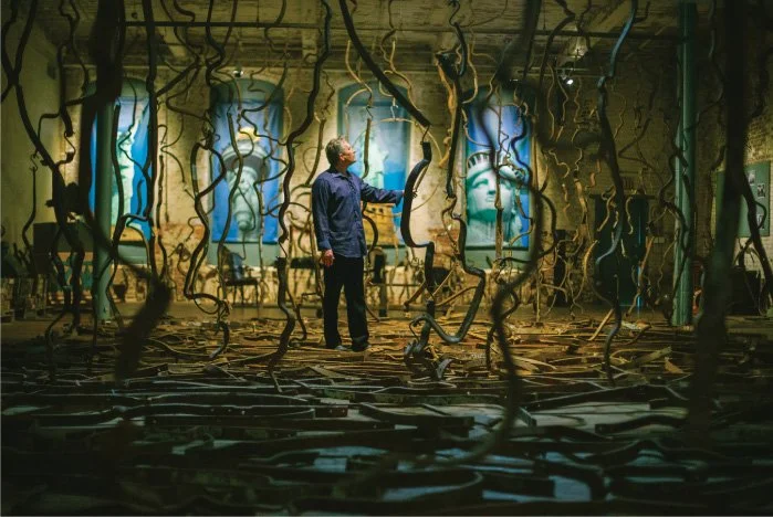 A man standing inside an art installation with tangled wires, looking at blue artwork depicting the Statue of Liberty and other figures.