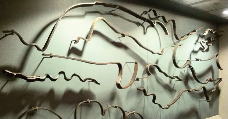 An art installation on a wall made of various twisted metal rods of different lengths and shapes, casting shadows.