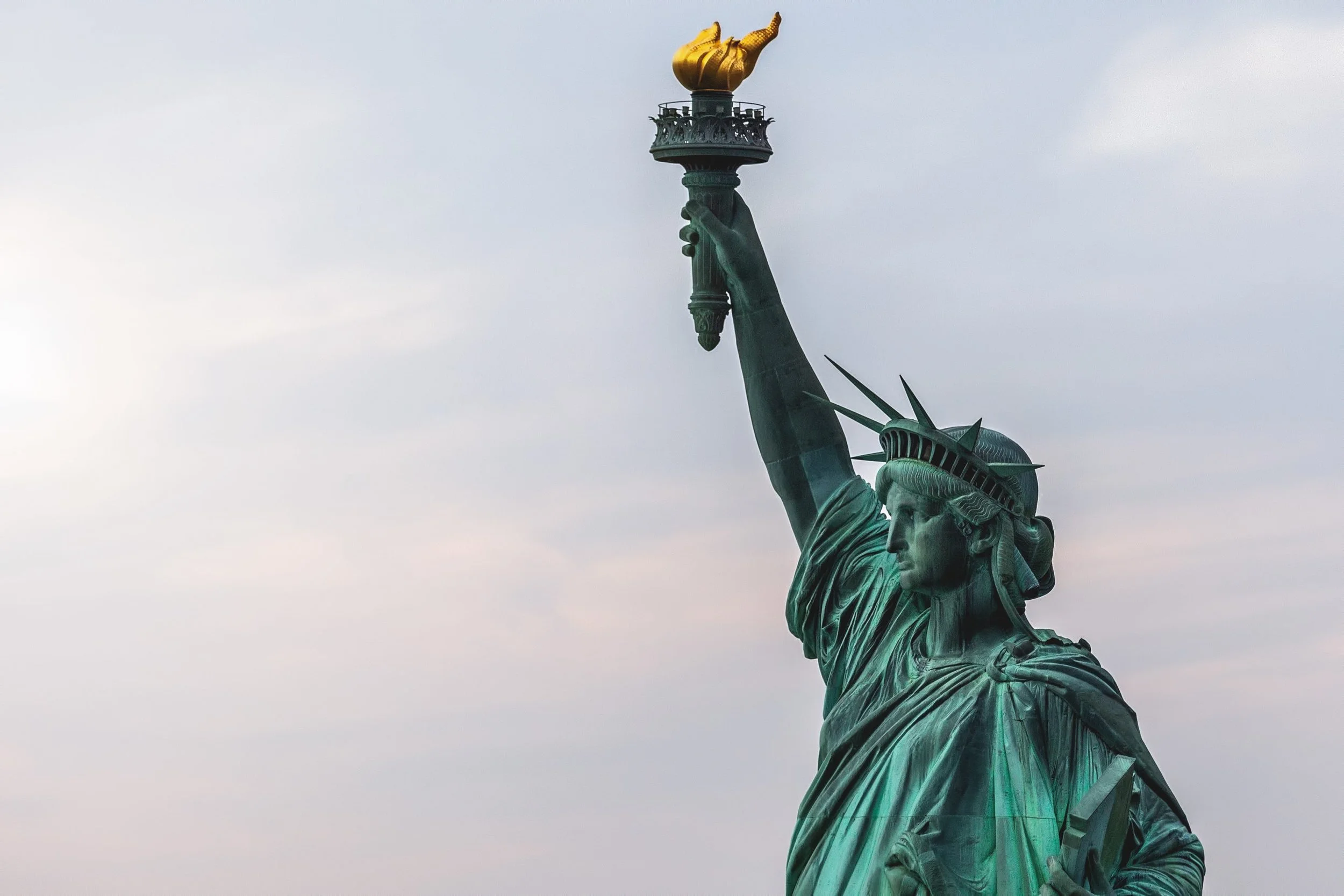 Close-up of the Statue of Liberty holding her torch high against a cloudy sky.