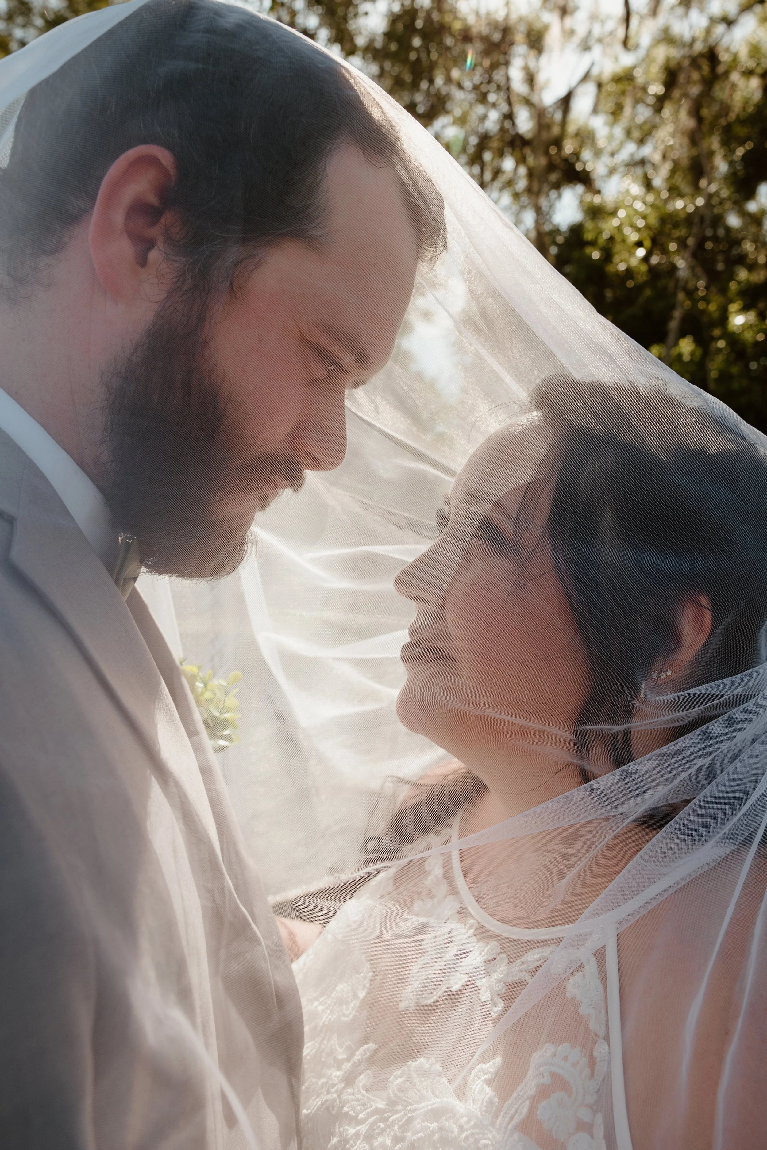 A man in a white cowboy hat and plaid shirt sitting on a rock, holding hands with a woman in a white t-shirt and jeans, smiling at each other outdoors in a garden with trees and rocks.