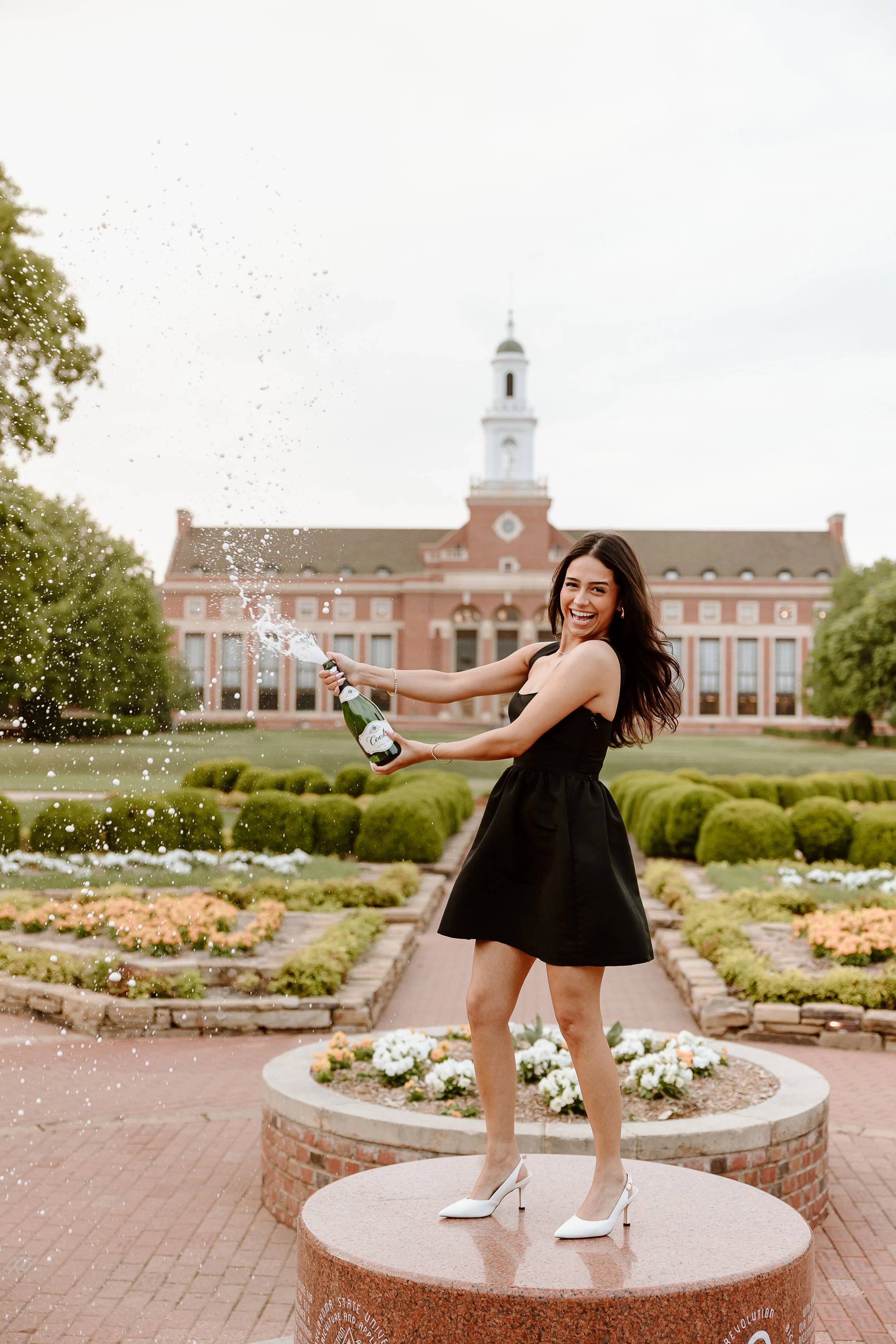 A young man in graduation attire hugging an older woman outdoors on a sunny day.
