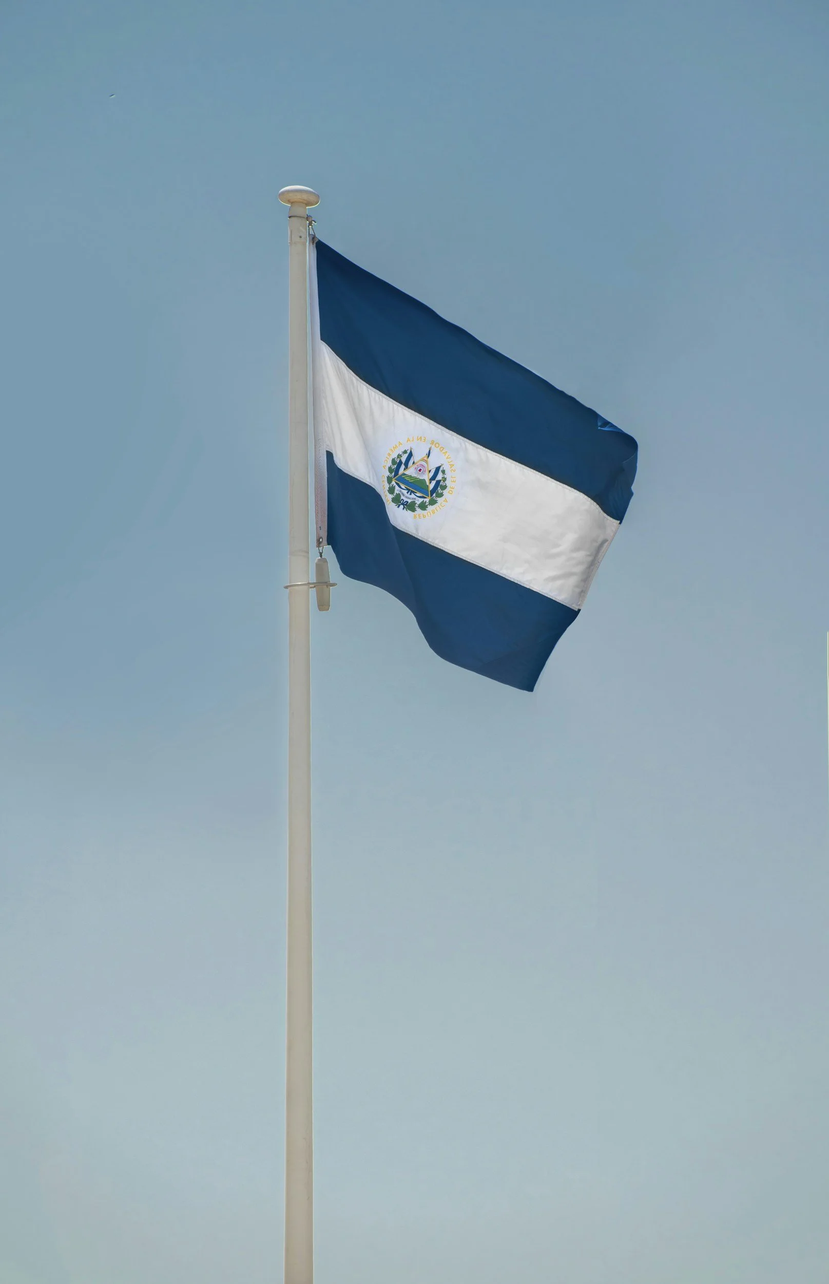 El Salvador flag on pole against blue sky backdrop.