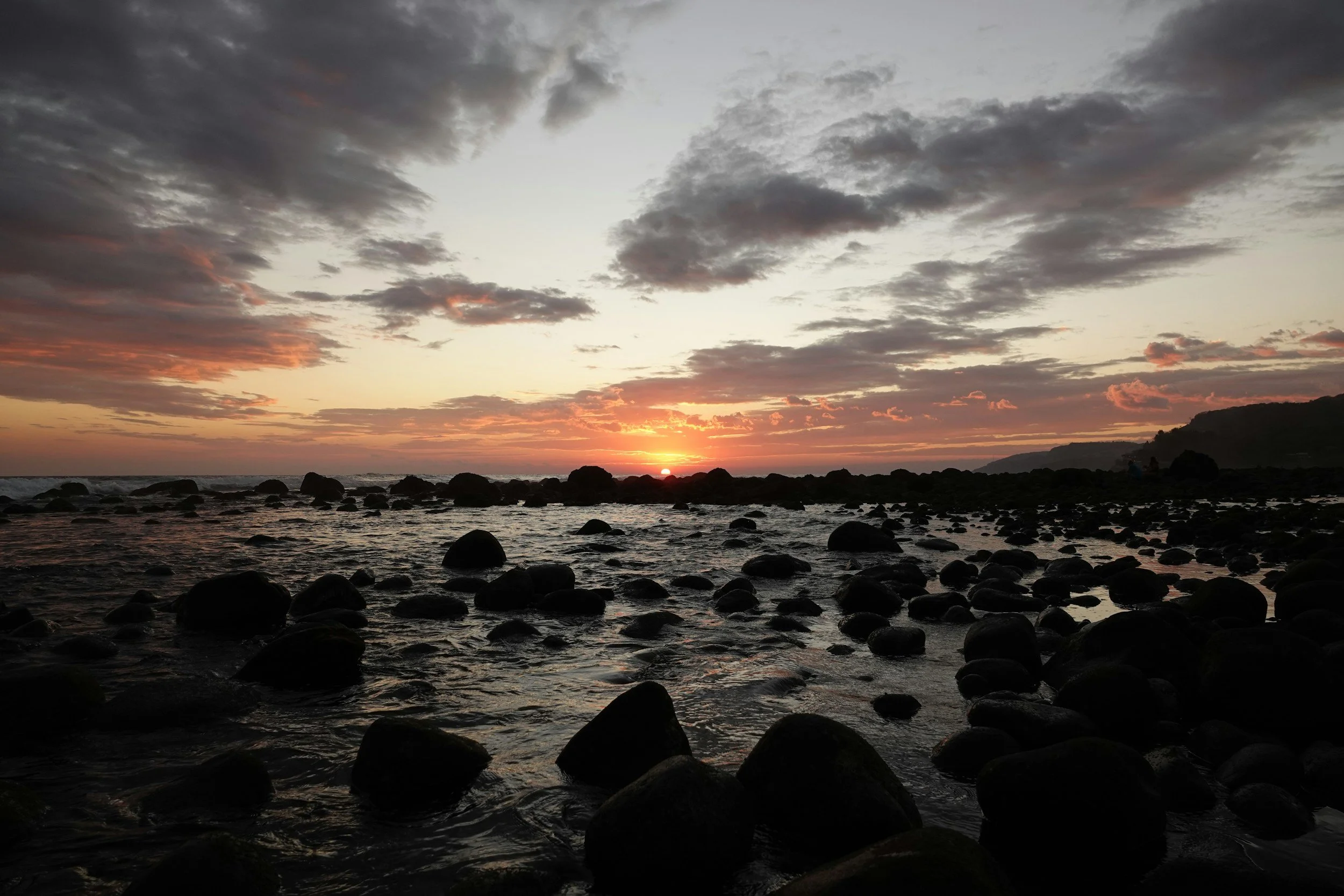 Rocky beach with sunset in the distance.