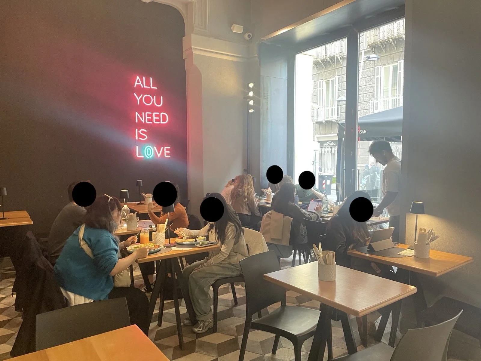 Cafe interior with tables, chairs, and bright "all you need is love" light signage.
