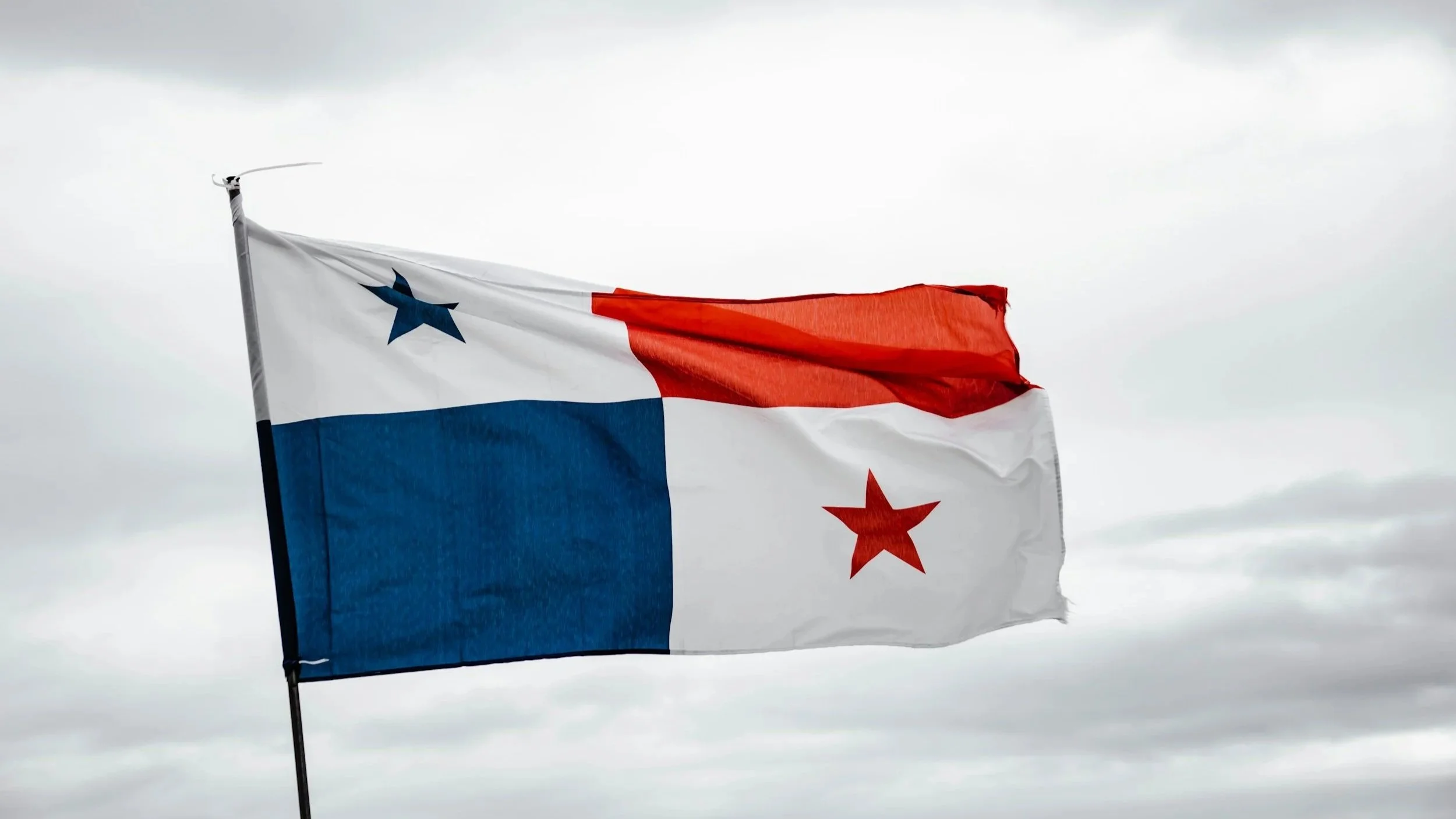 Panama flag waving on pole with cloudy sky backdrop.
