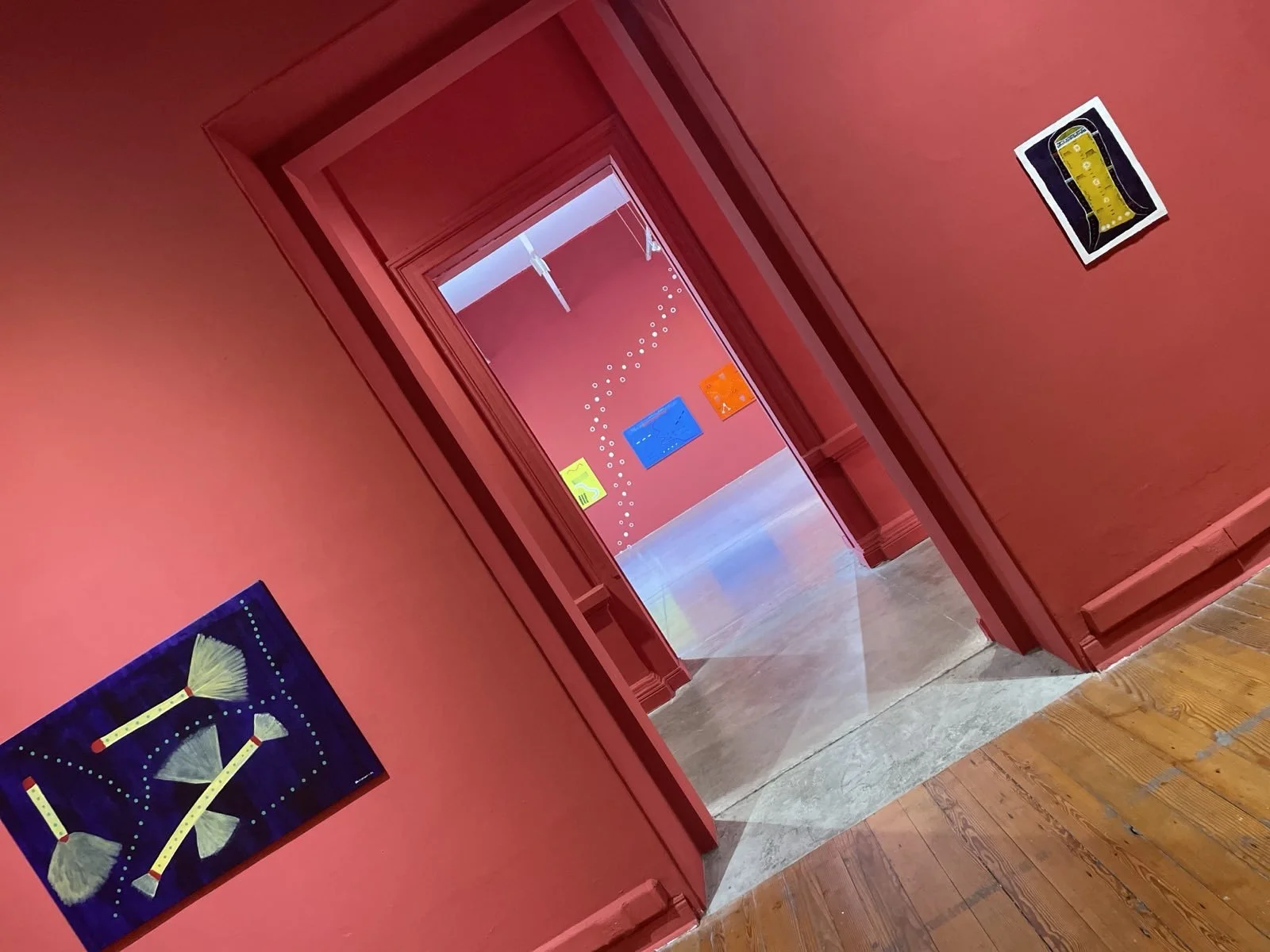 Slanted view through doorway of red rooms with colourful wall art.