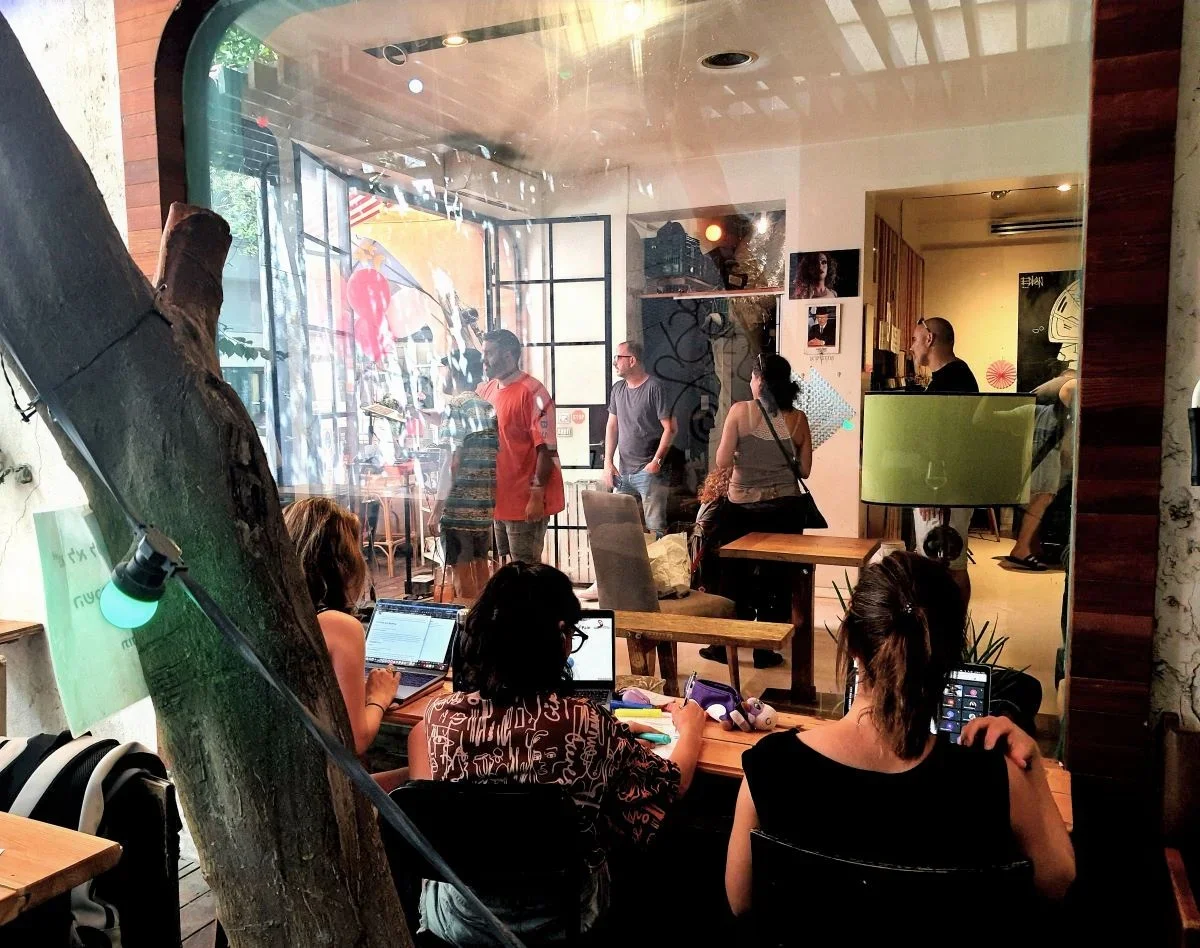Cafe interior with people sitting, having coffee, on laptops, standing around, etc.