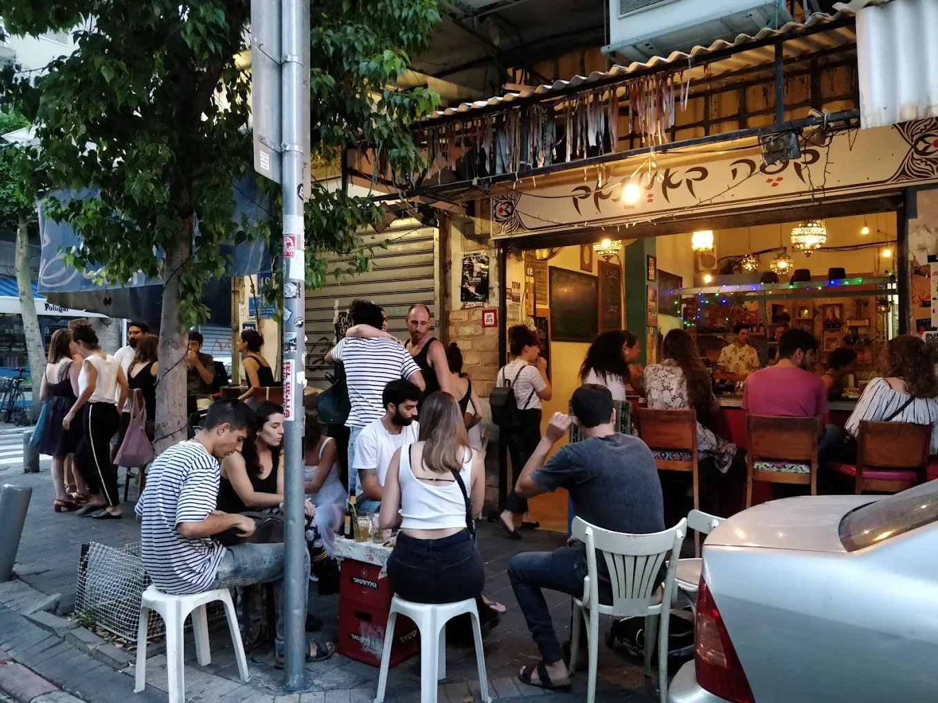 Bustling scene with many people sitting and standing outside a cafe in Tel Aviv.