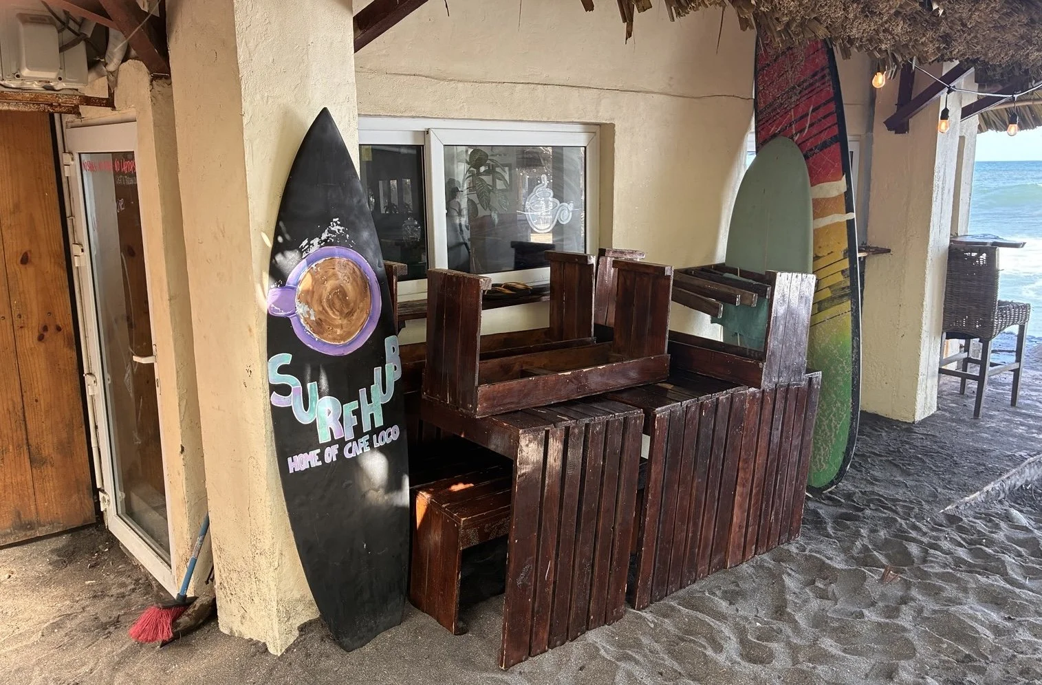 Exterior of "Surfhub" beach cafe with black and purple surfboard signage.