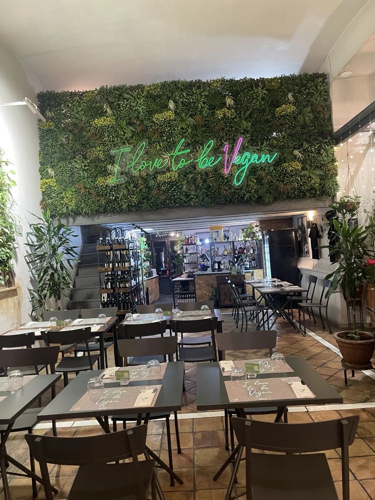 Vegan restaurant interior with tables, chairs, and "I love to be vegan" light signage.